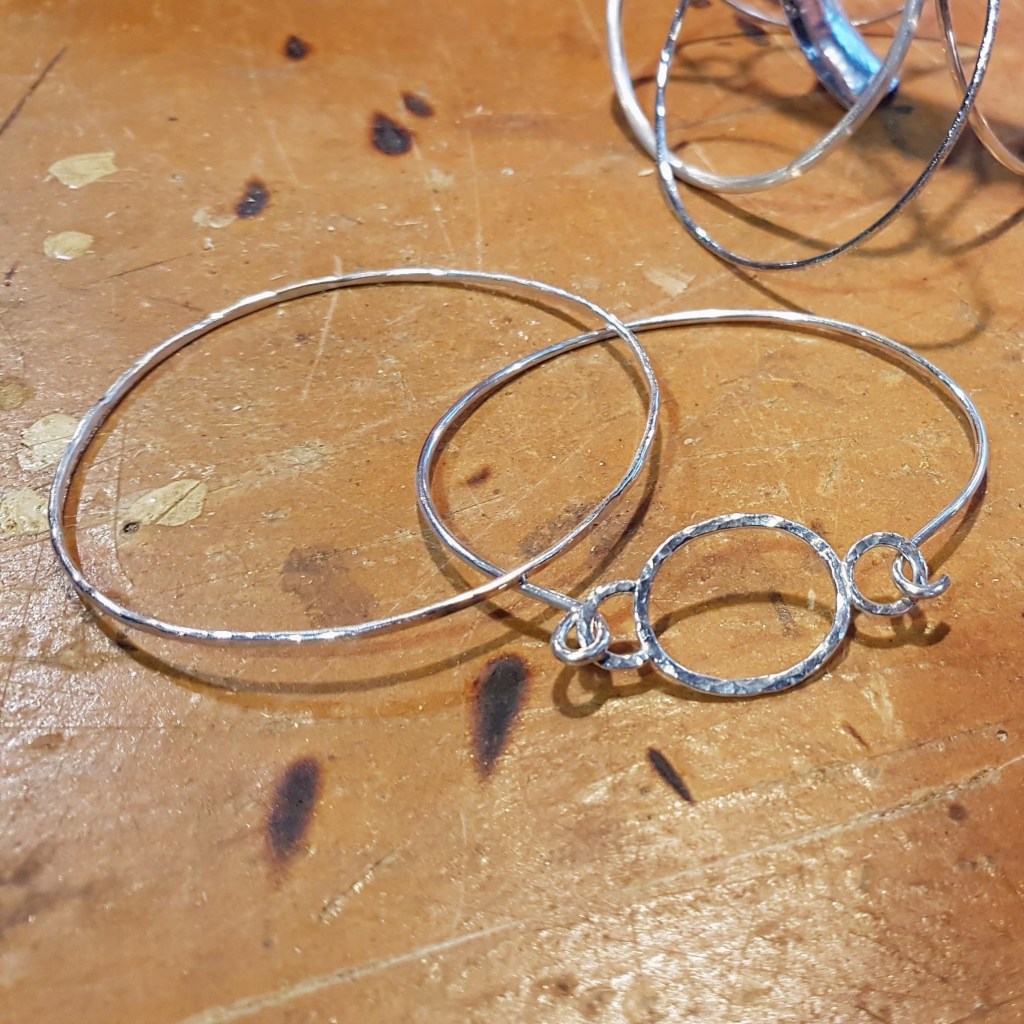 Close-up of silver hoop earrings and a bracelet with a circular pendant on a wooden surface.